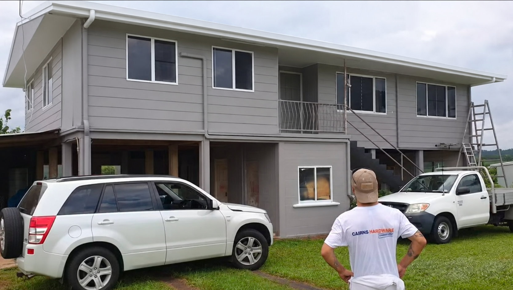Painter standing with his back to the camera, looking at a Queensland house; gutter finish digitally enhanced