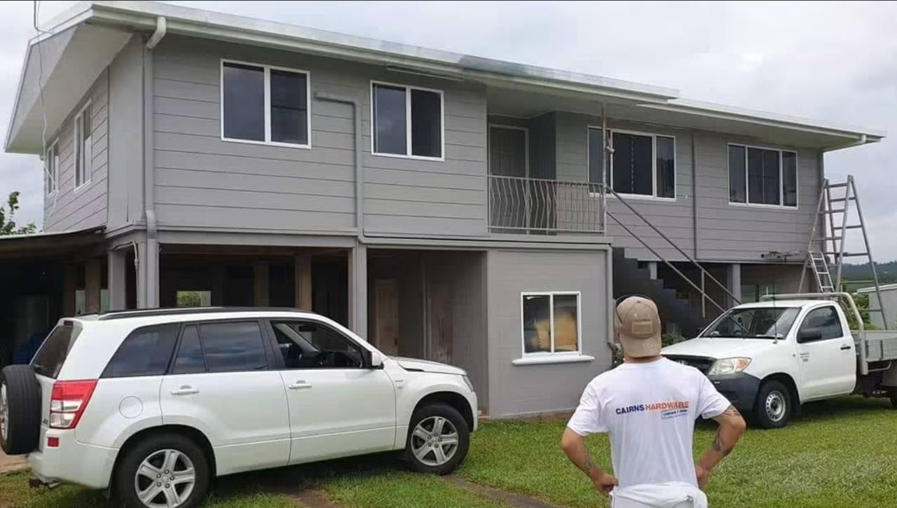 Painter standing with his back to the camera, looking at a freshly painted Queensland house
