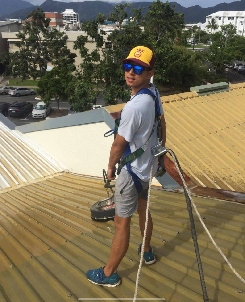 Worker wearing a harness with cleaning equipment on a metal roof in Cairns